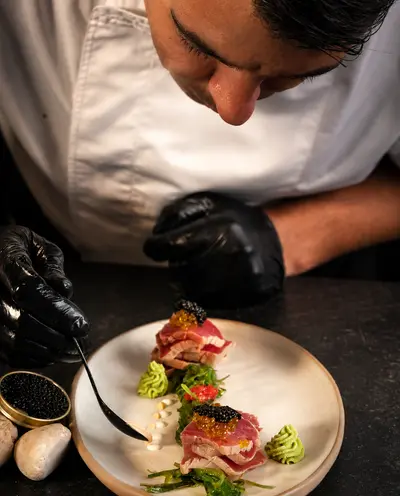 Chef con guantes negros terminando un plato con caviar